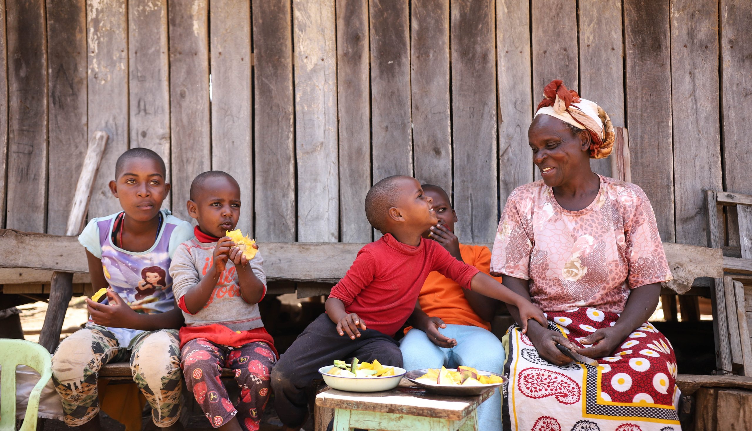 Die kenianische Bäuerin Faith Wanjiru sitzt mit ihren Enkeln auf der Bank. Gemeinsam geniessen sie frische Früchte.
