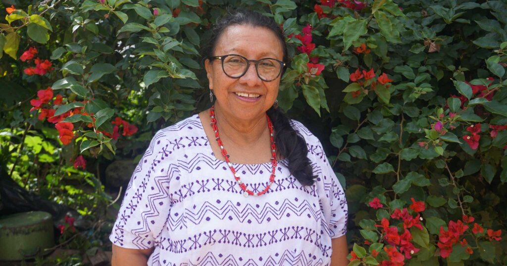 Inés Pérez, Koordinatorin in Guatemala, steht vor einer blühenden Hecke.